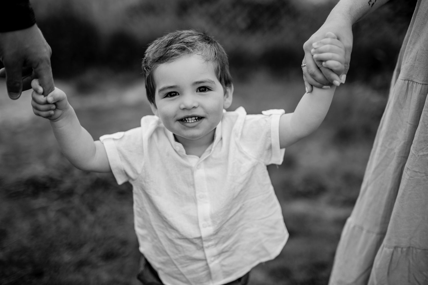 Black and white portrait of a young child holding hands and smiling outdoors.