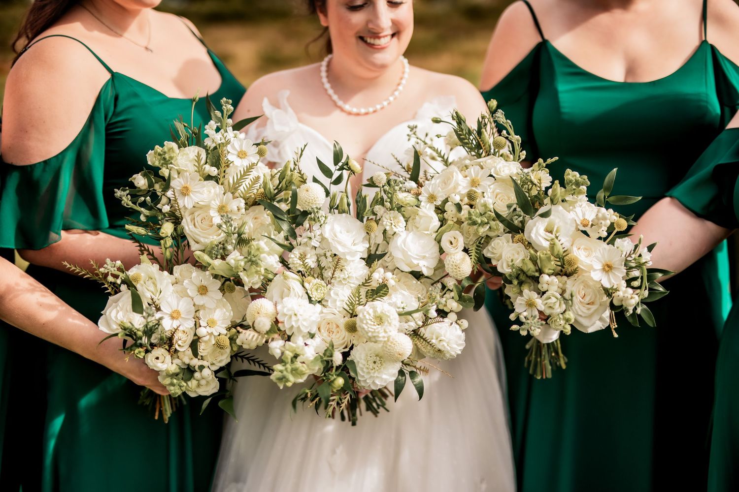 Close-up of elegant white and green wedding bouquets against emerald dresses.