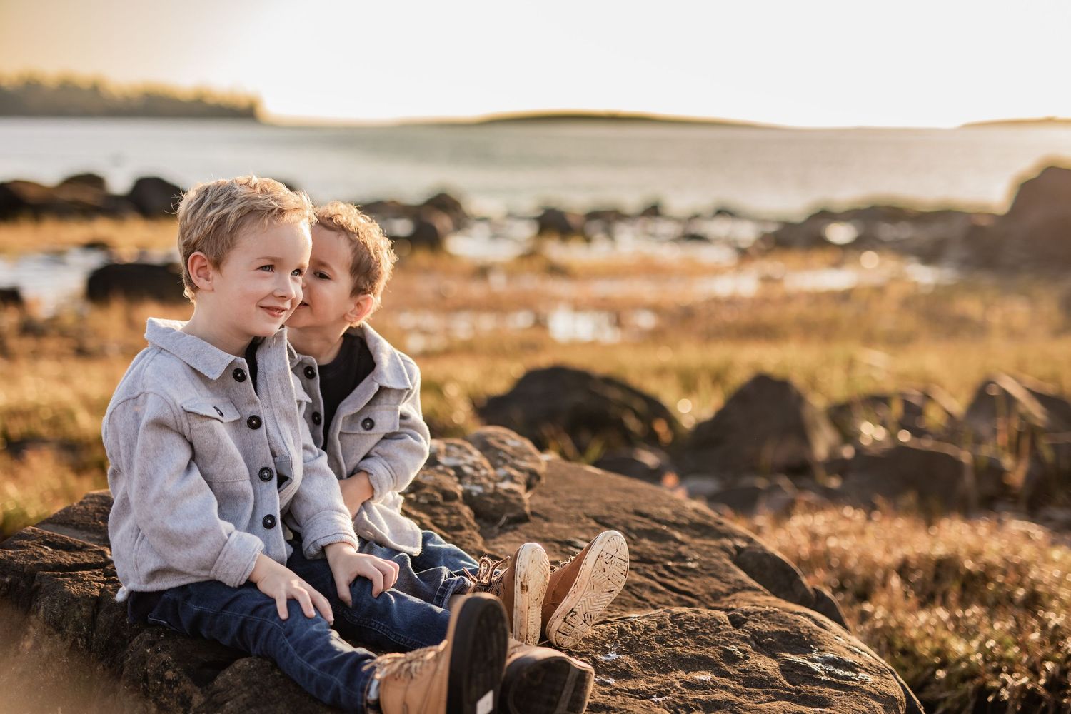 Siblings sitting together on coastal rocks during a sunset photoshoot.