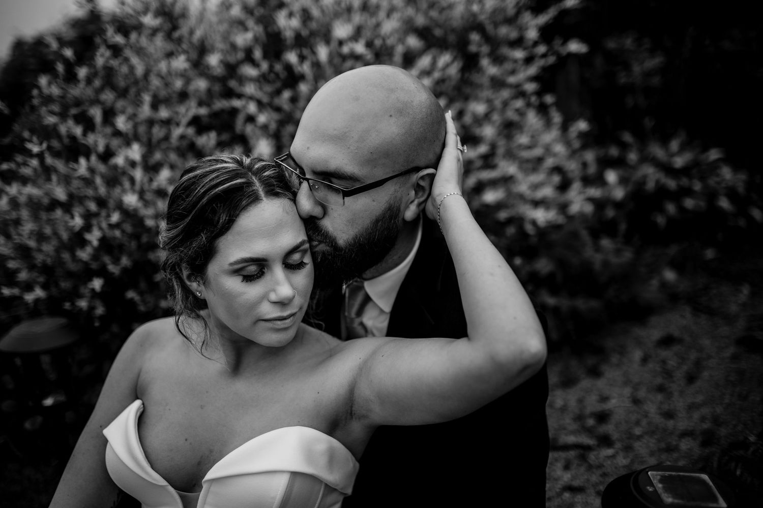 Artistic black and white portrait of couple in romantic embrace outdoors.