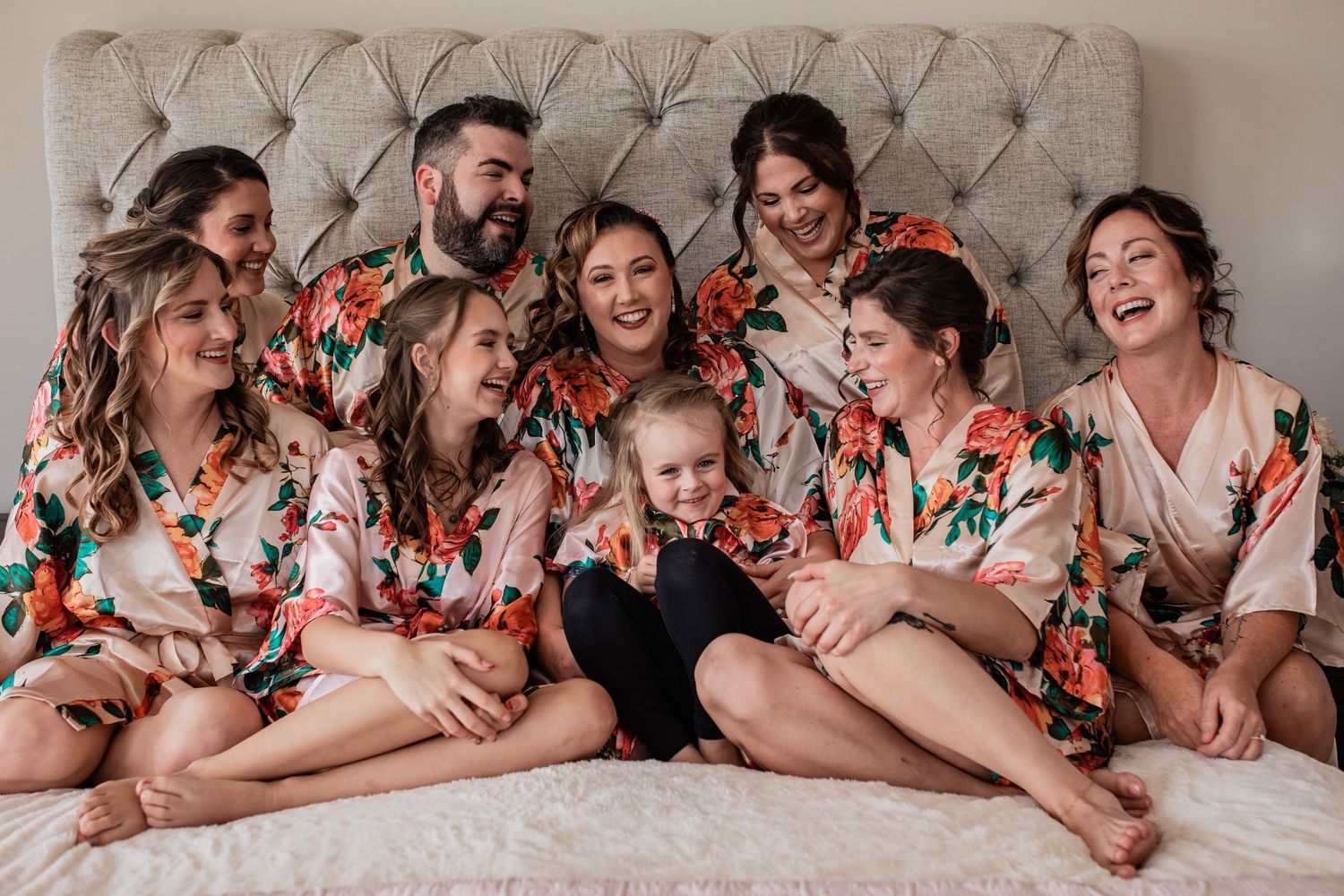 Group wearing coordinated floral robes poses together on gray tufted headboard.
