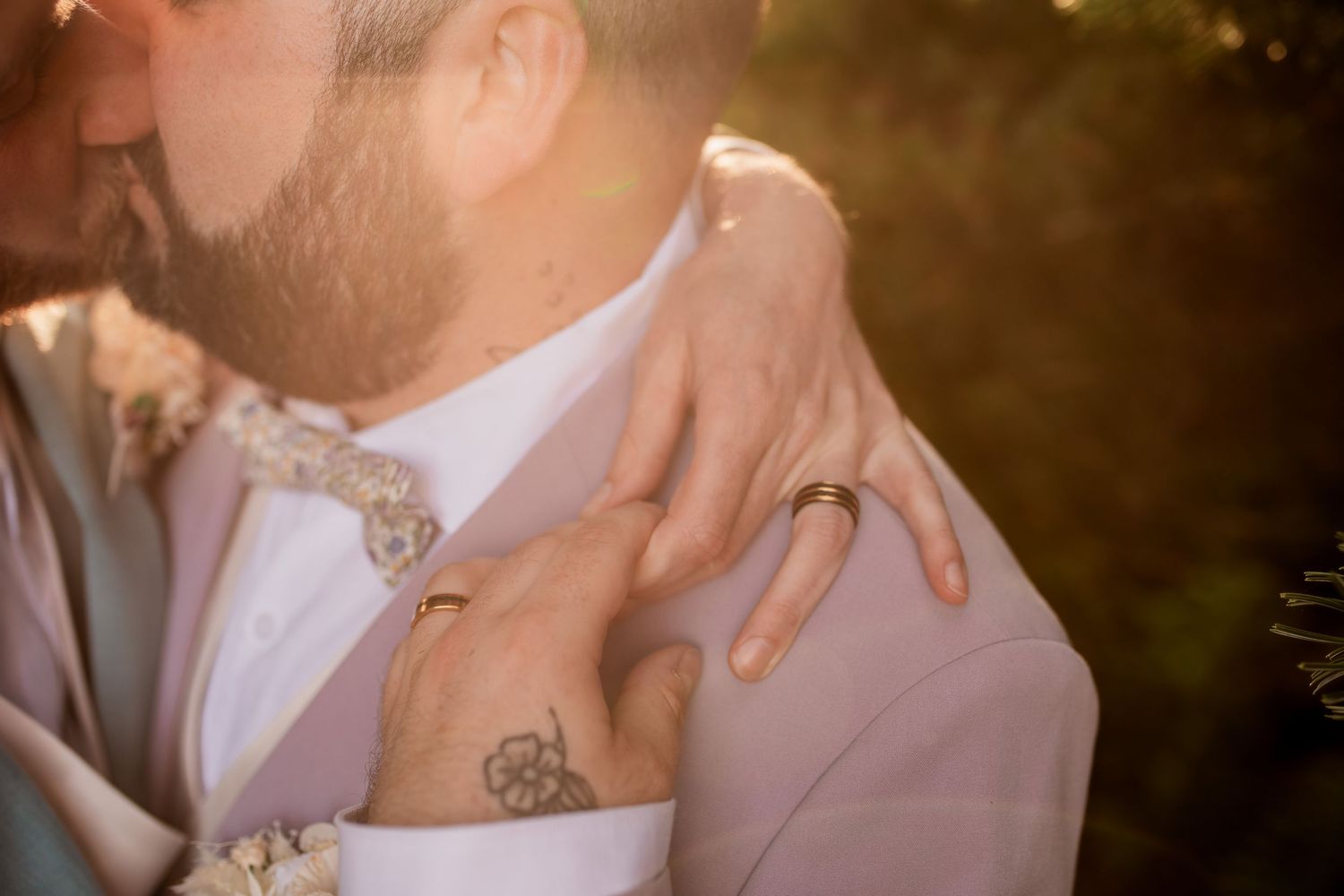 Close-up of hands with tattoos embracing during sunset wedding moment.