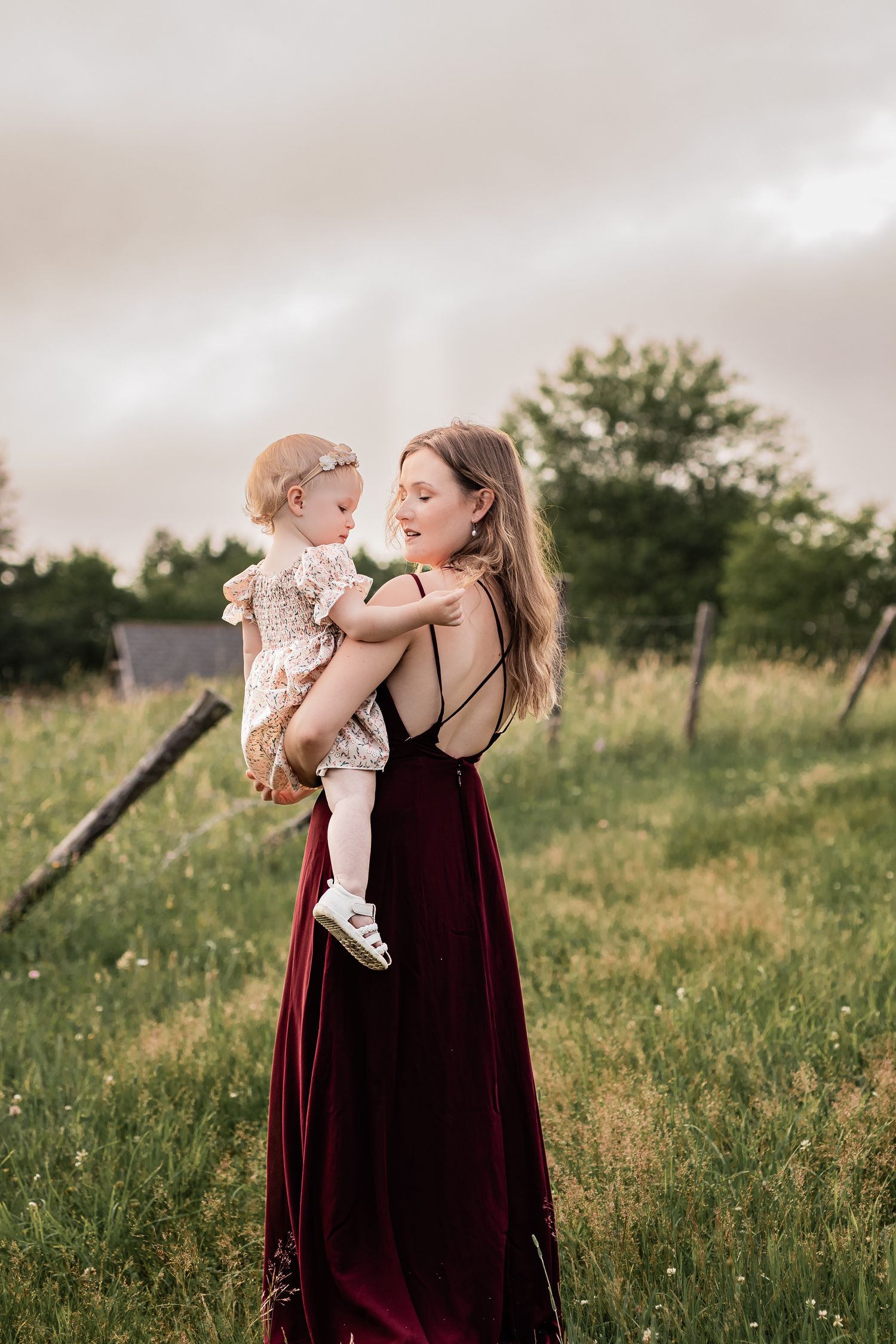A tender moment shared between parent and child in a burgundy dress against a sunset meadow backdrop.