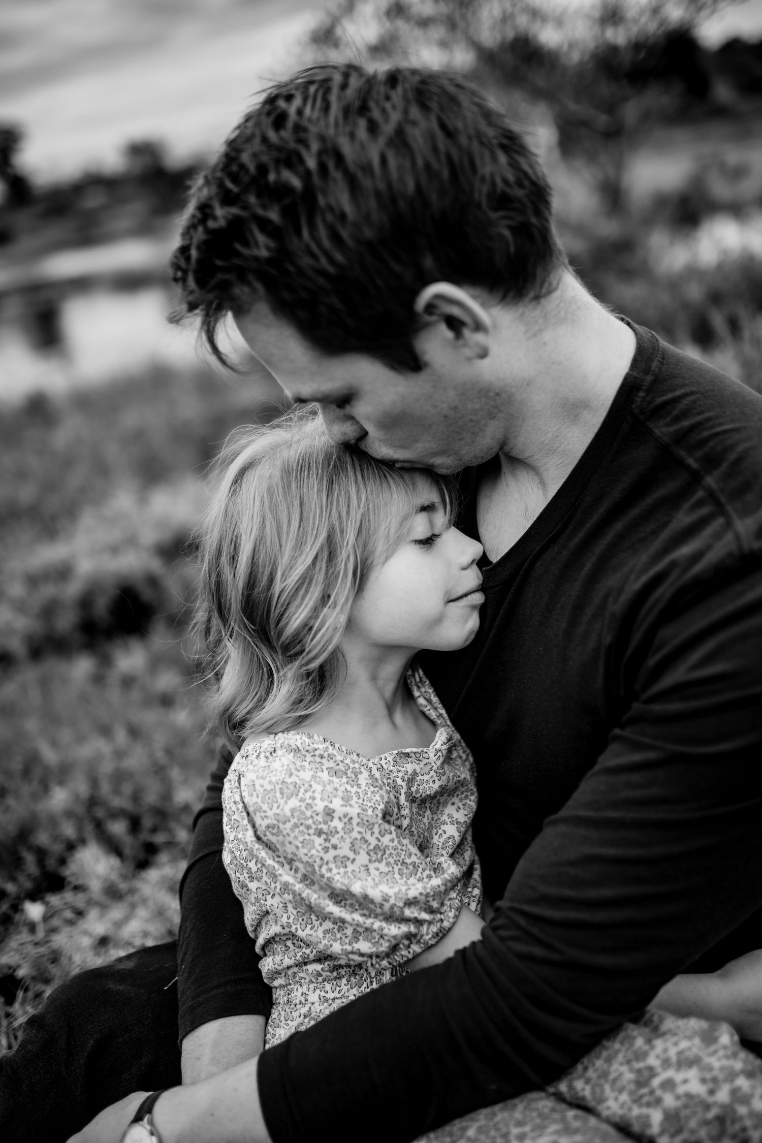 Tender black and white portrait of parent and child sharing an intimate moment outdoors.