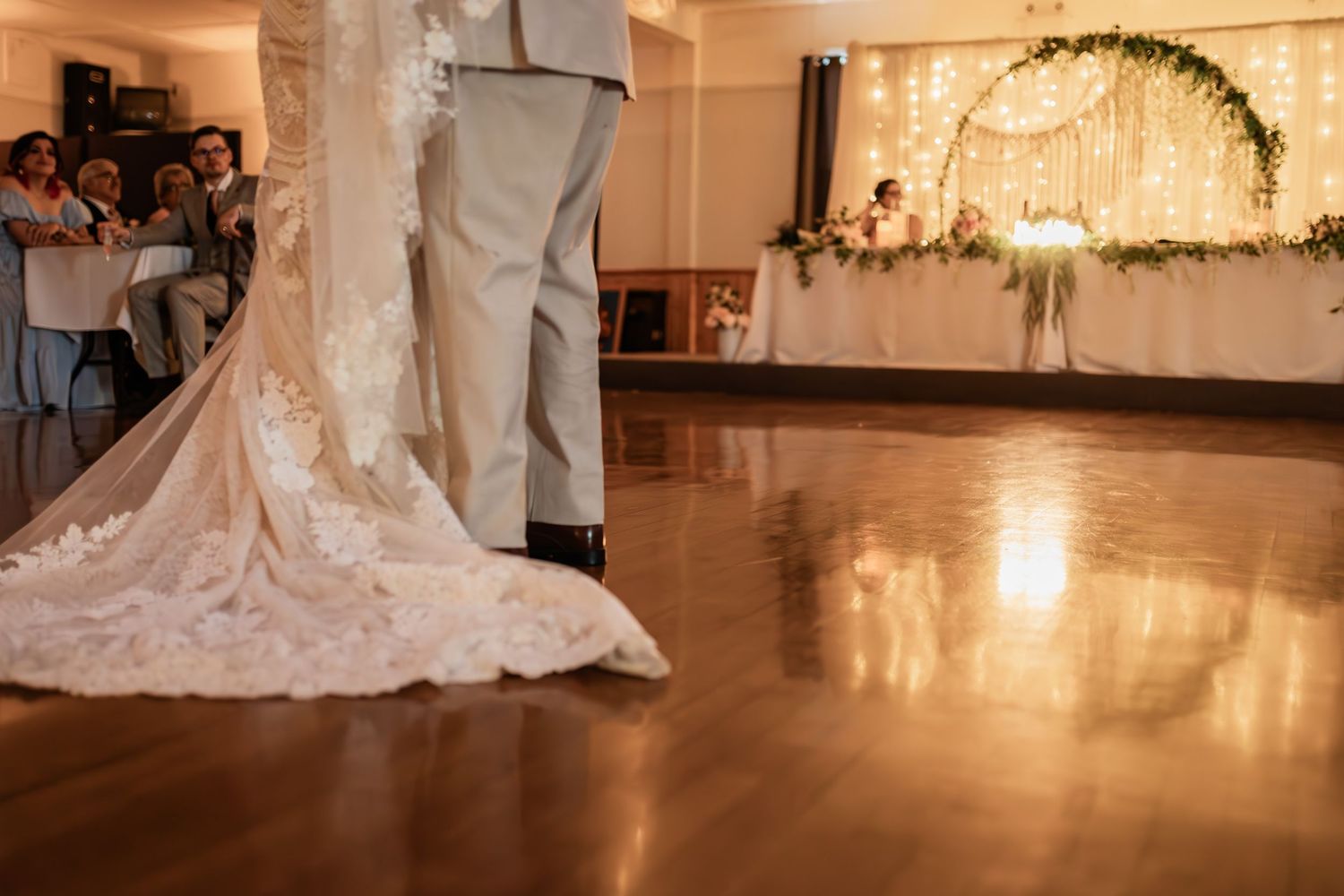 A wedding dress train trails across a polished ballroom floor during a reception dance.