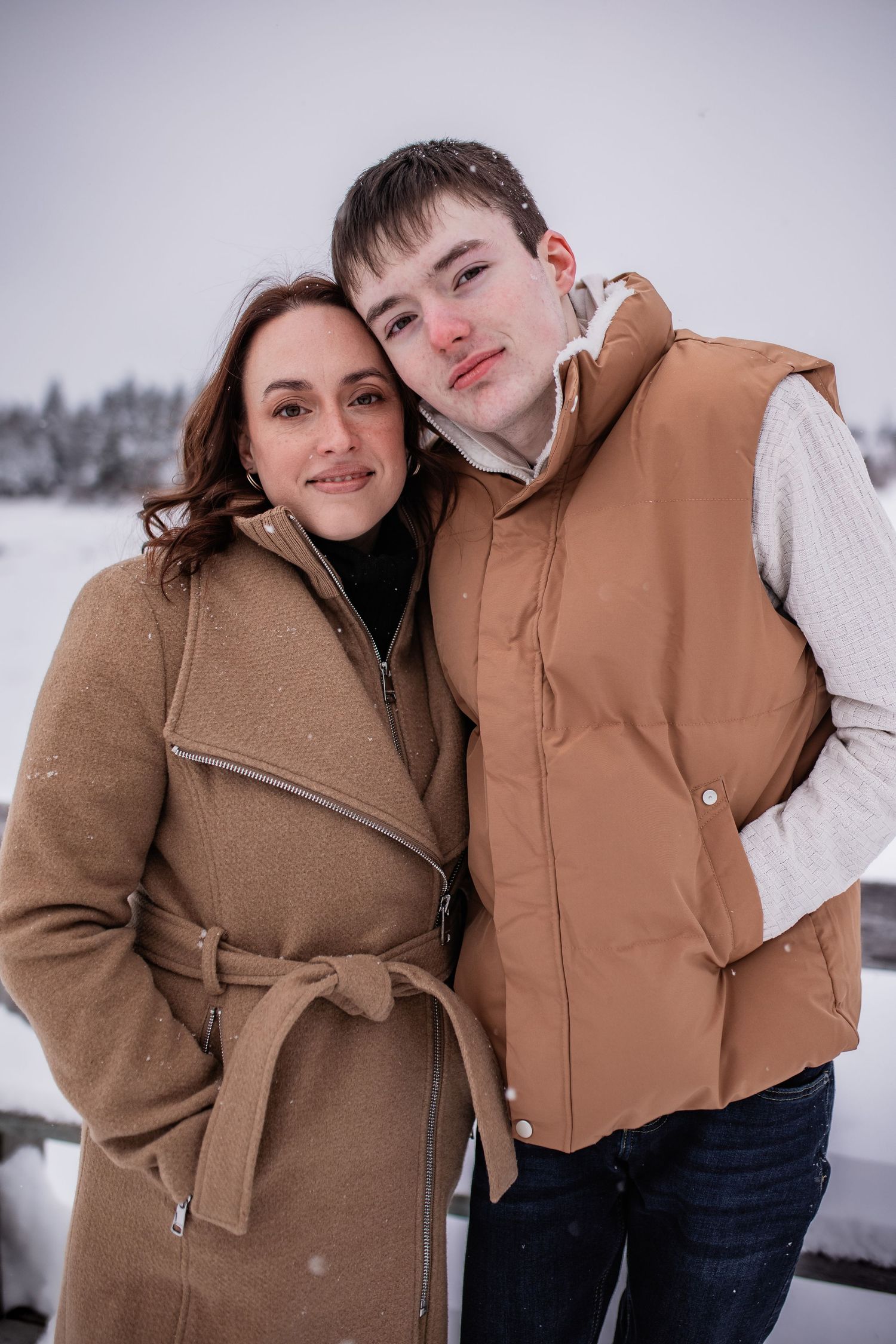 Winter portrait of two people in warm coats posing together in the snow.
