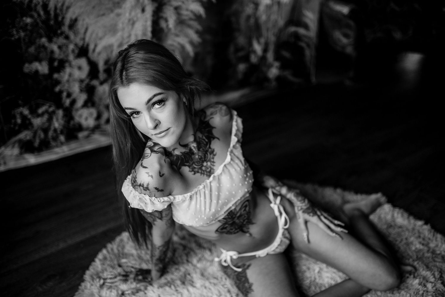 Monochrome boudoir photograph with vintage-style white lace lingerie on textured carpet.