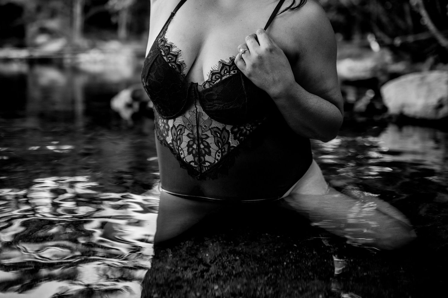 Black and white artistic photograph of a person in a lace corset sitting in dark reflective water.