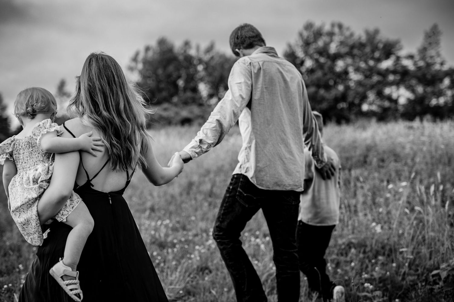 Black and white portrait of a family enjoying playful moments in a field.