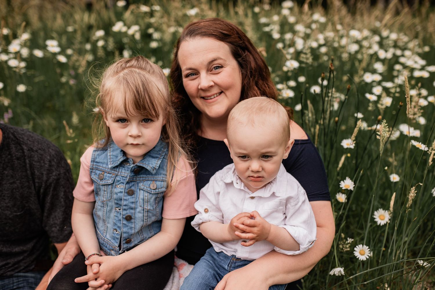 Family sits together in blooming daisy field during summer.