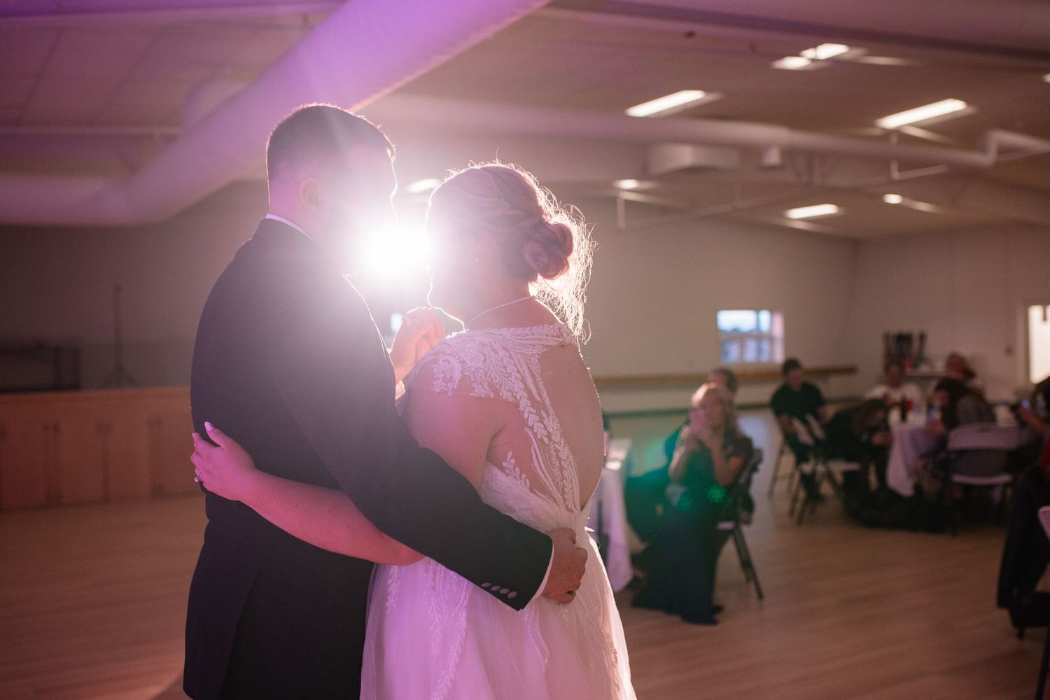 Silhouetted couple embraces during wedding dance with soft backlight glow.
