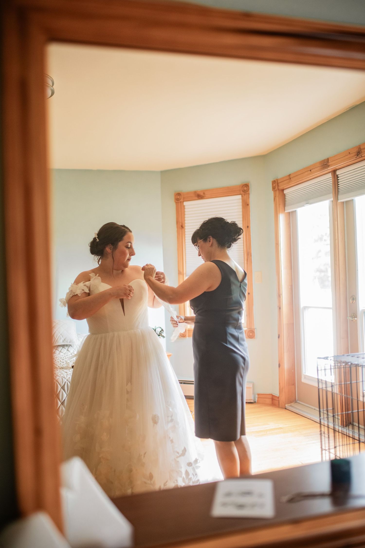 A tender getting-ready moment reflected in a mirror with warm lighting and wooden frames.