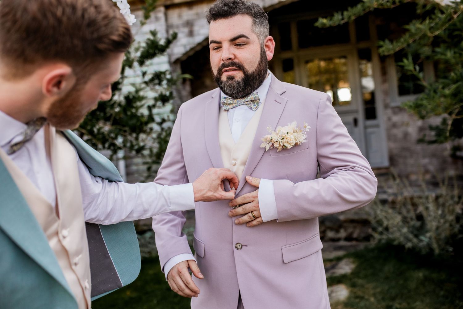 Groomsmen in pastel suits helping with boutonniere during wedding preparation.
