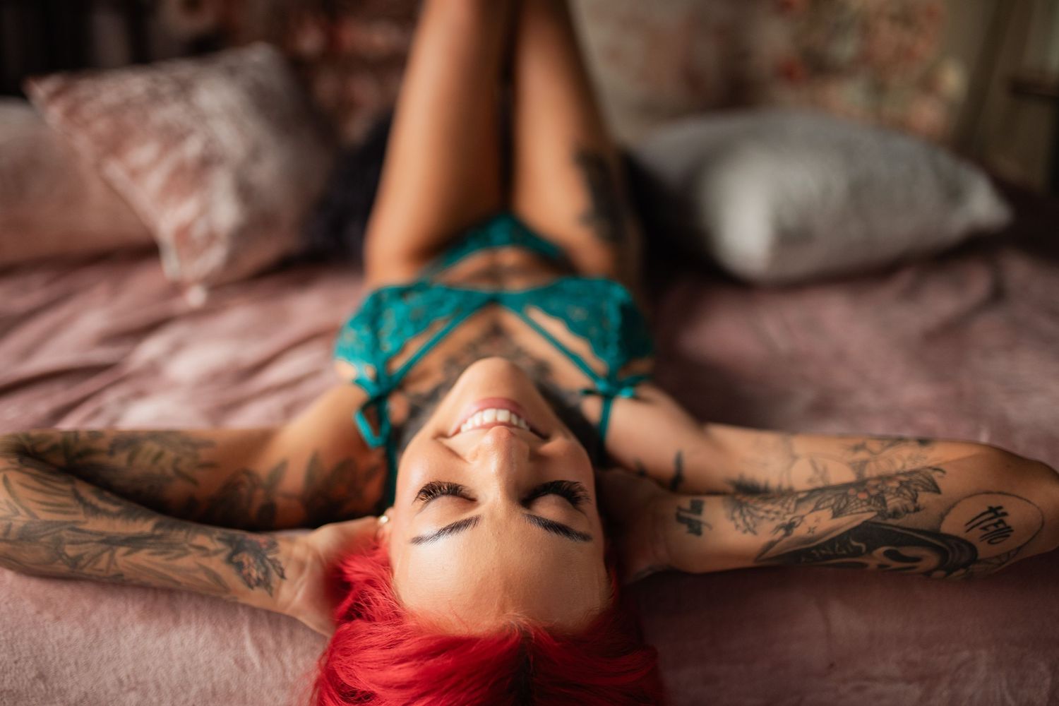 Intimate portrait of tattooed person with red hair lying on pink bedding.