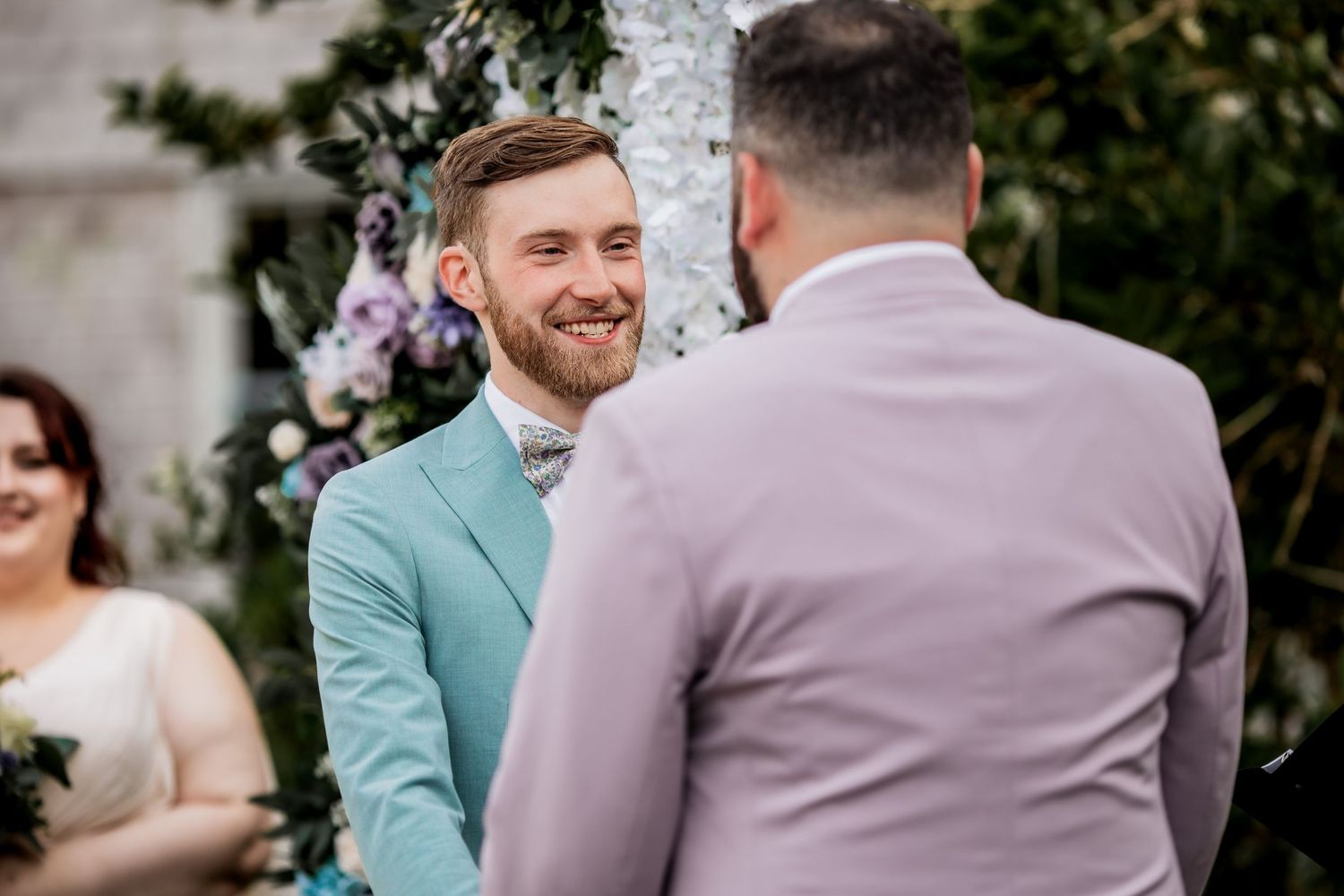 Two people in mint green and lavender suits share joyful moment at outdoor ceremony.