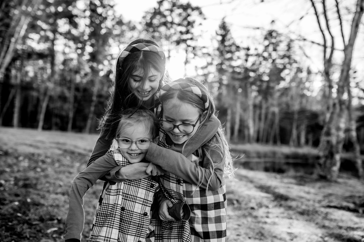 Happy family wearing matching plaid shirts embraces and laughs together in an autumn forest setting.