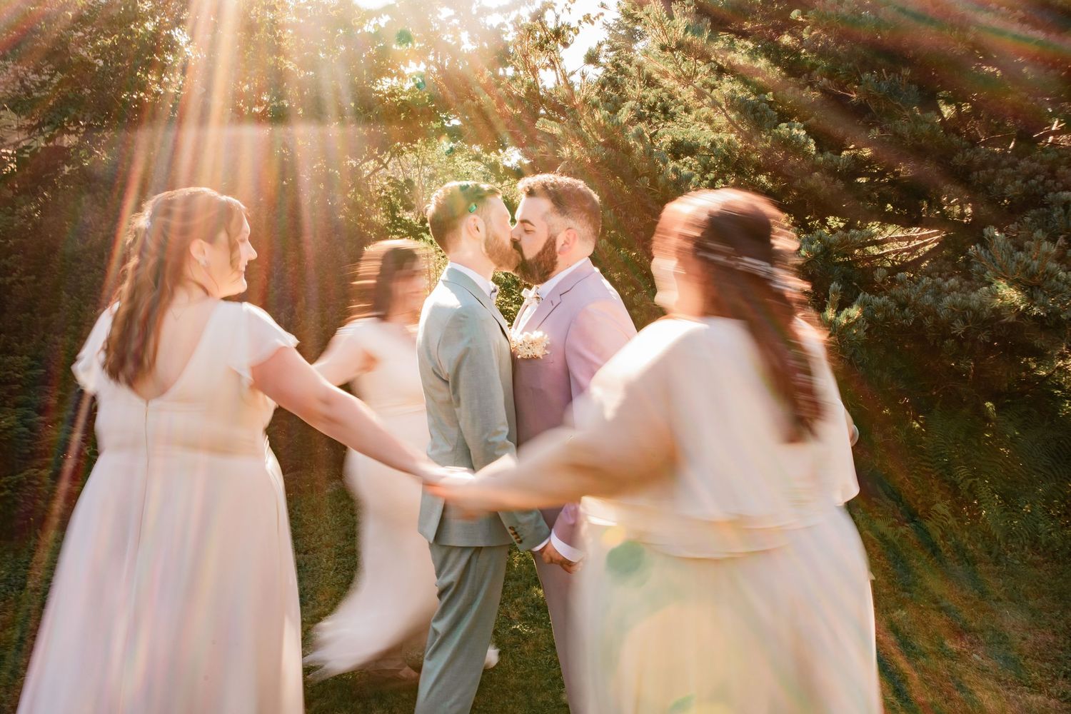 Wedding party celebrates in garden with golden sunlight streaming through trees.