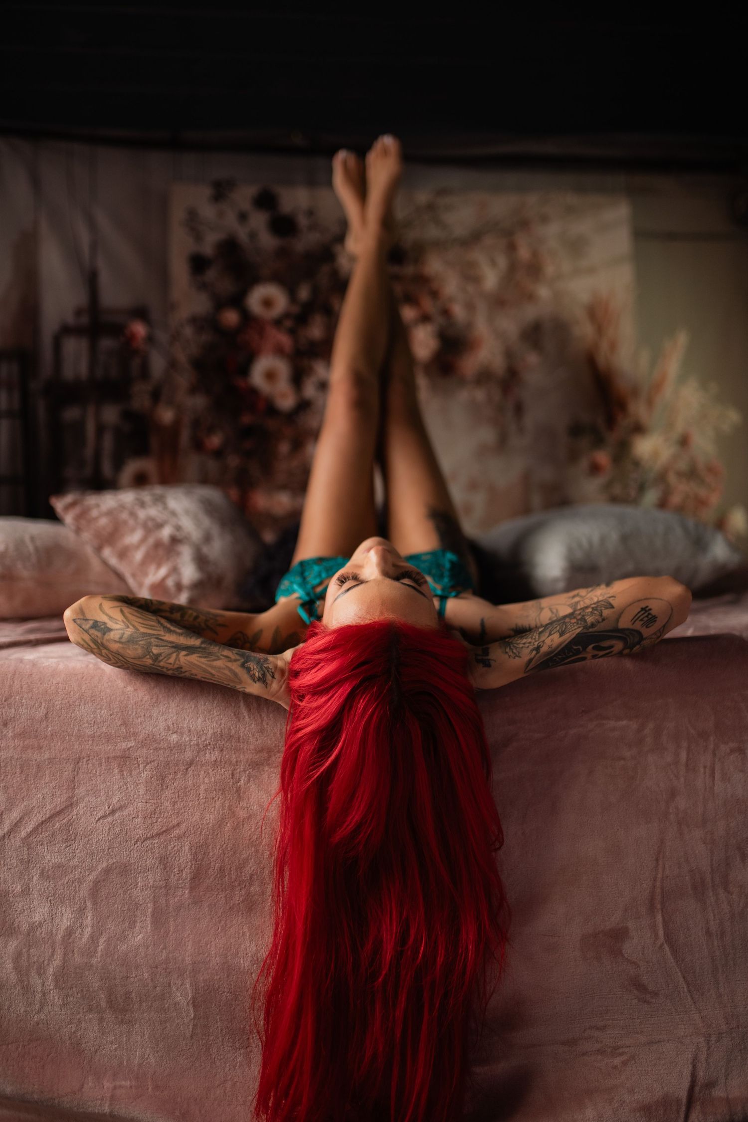 Person with long red hair laying back on pink bedding with arms stretched overhead.