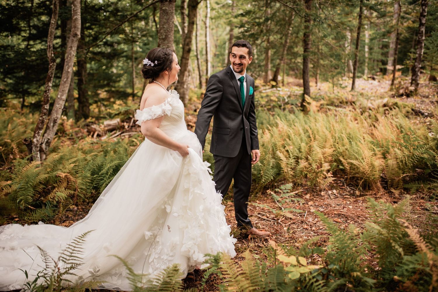 A romantic woodland wedding scene with ferns and evergreen trees in the background.
