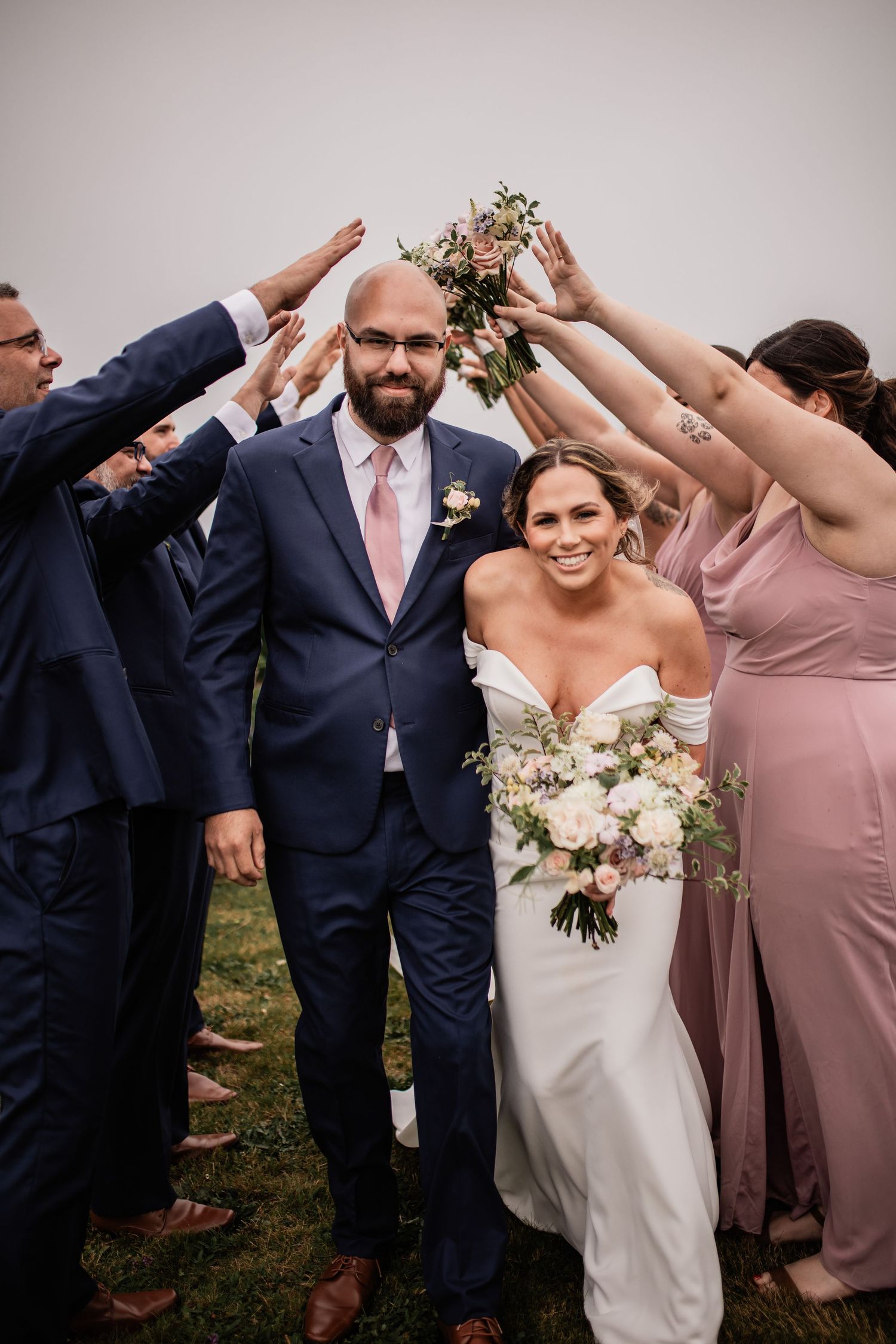 Wedding party forms celebratory arch with raised arms at outdoor ceremony.
