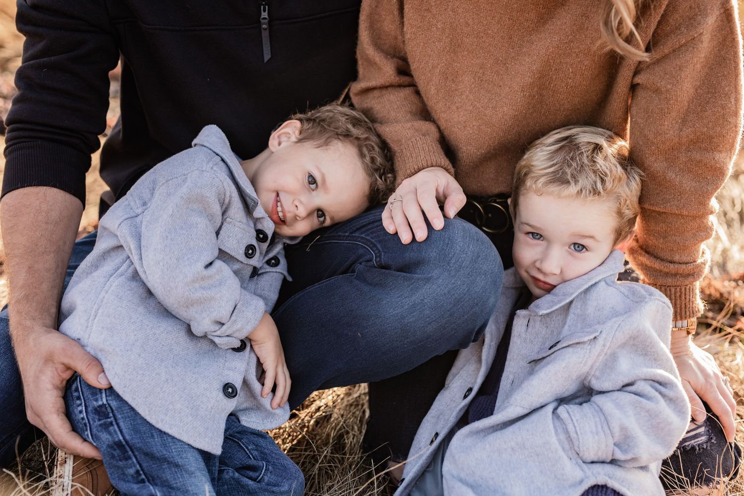 A casual outdoor portrait of three people relaxing together in matching gray jackets.
