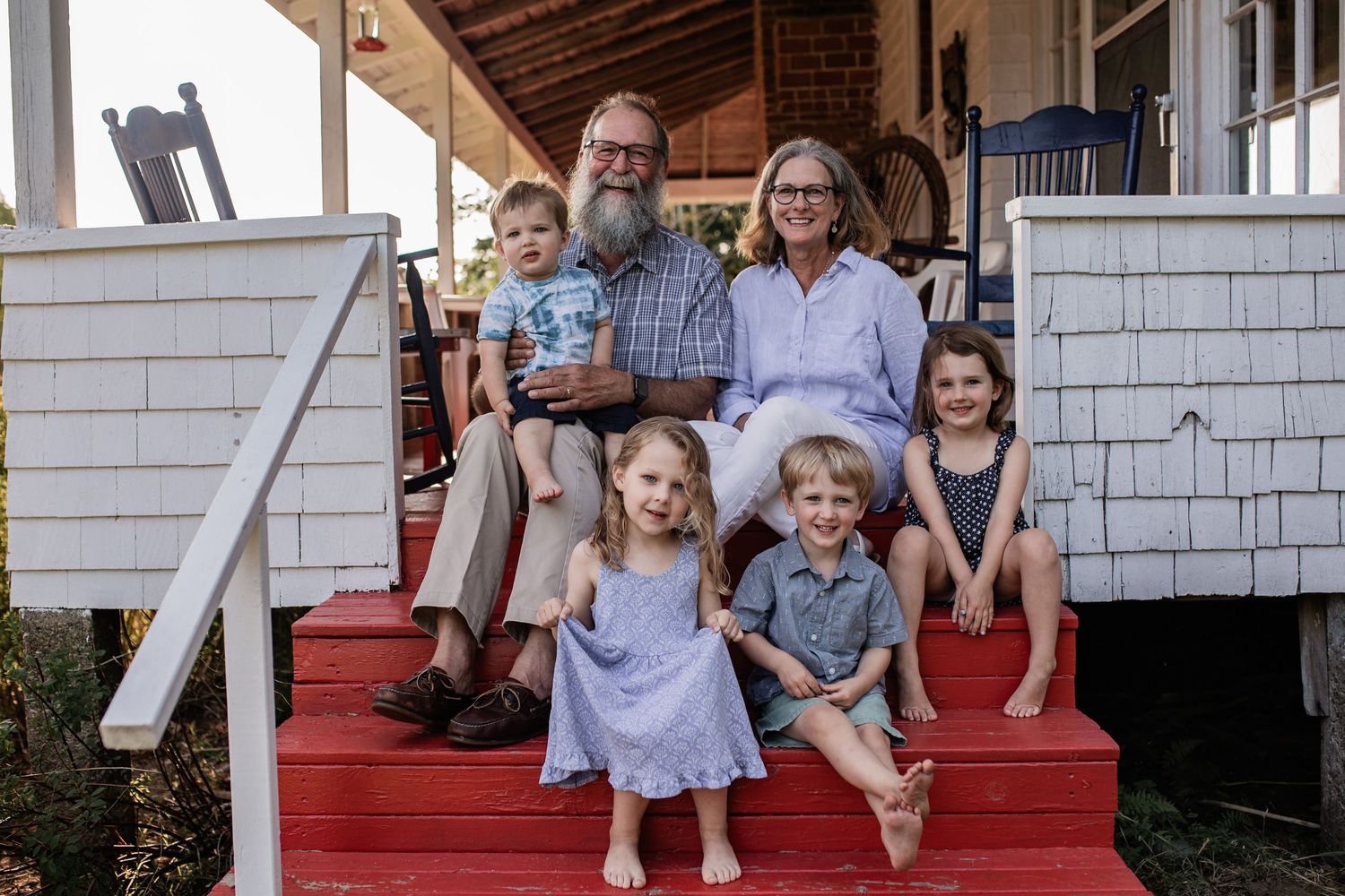 Multi-generational family portrait on red porch steps of a white craftsman style home.