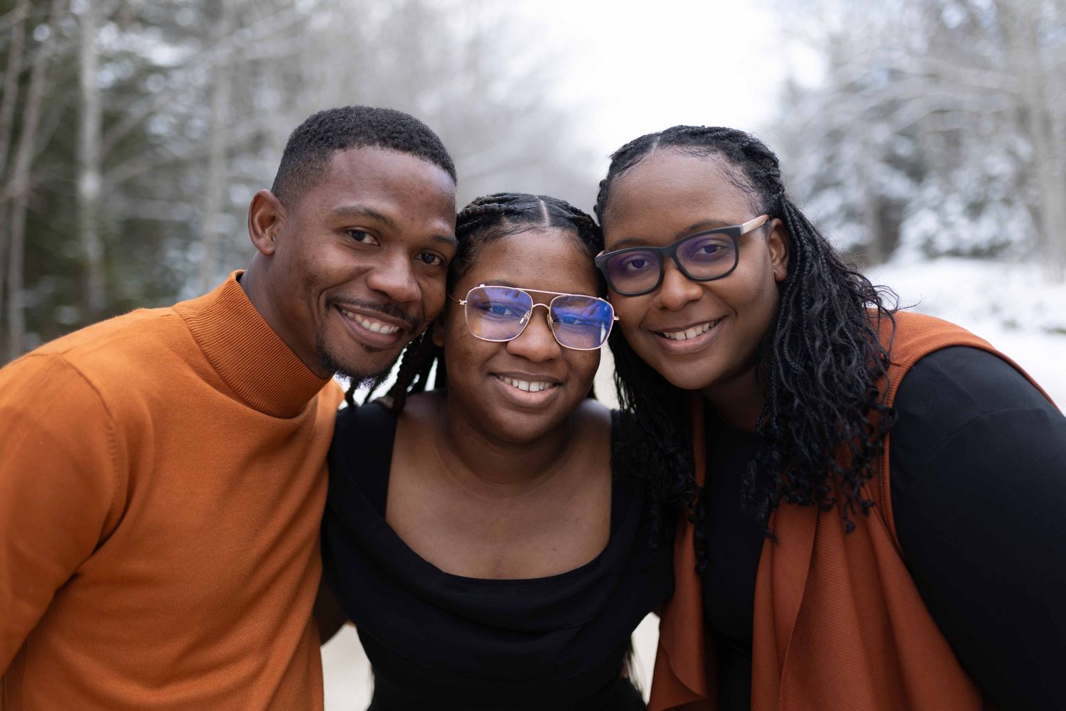 Three people smiling together in a close-up shot against a snowy winter background.