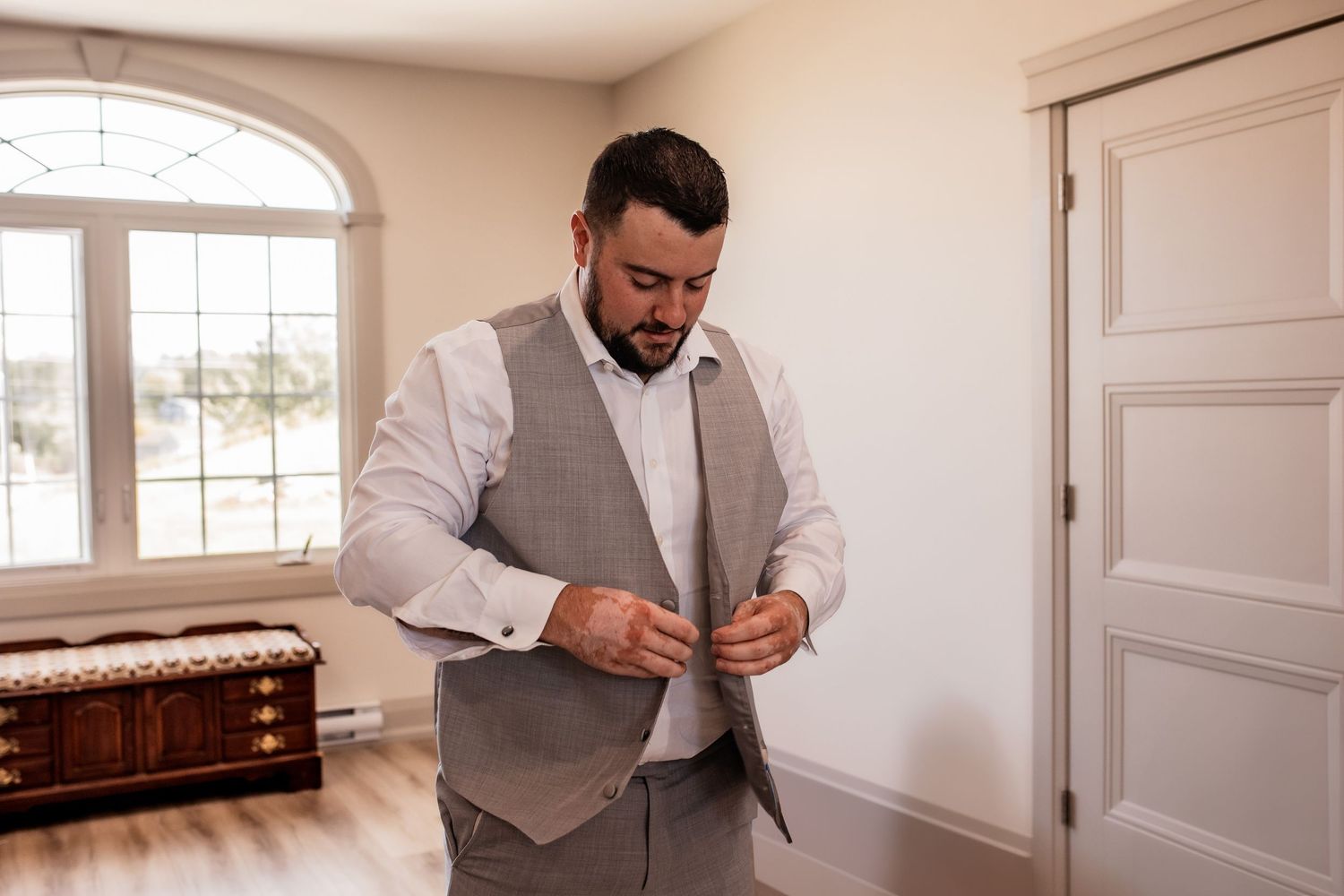 Groom in light gray vest and white shirt getting ready for wedding ceremony.