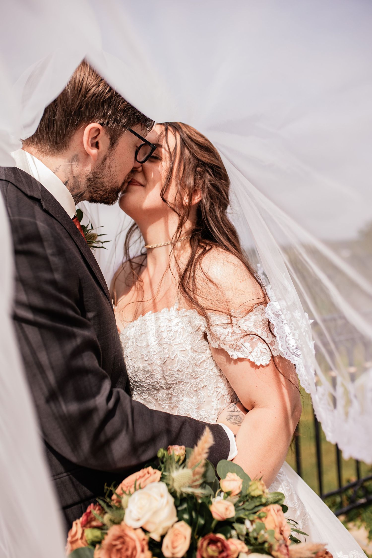 Romantic wedding couple sharing an intimate moment under a flowing veil with peach roses.