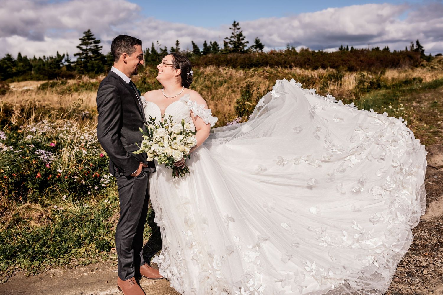 Wedding couple standing on trail with flowing lace dress spread out.