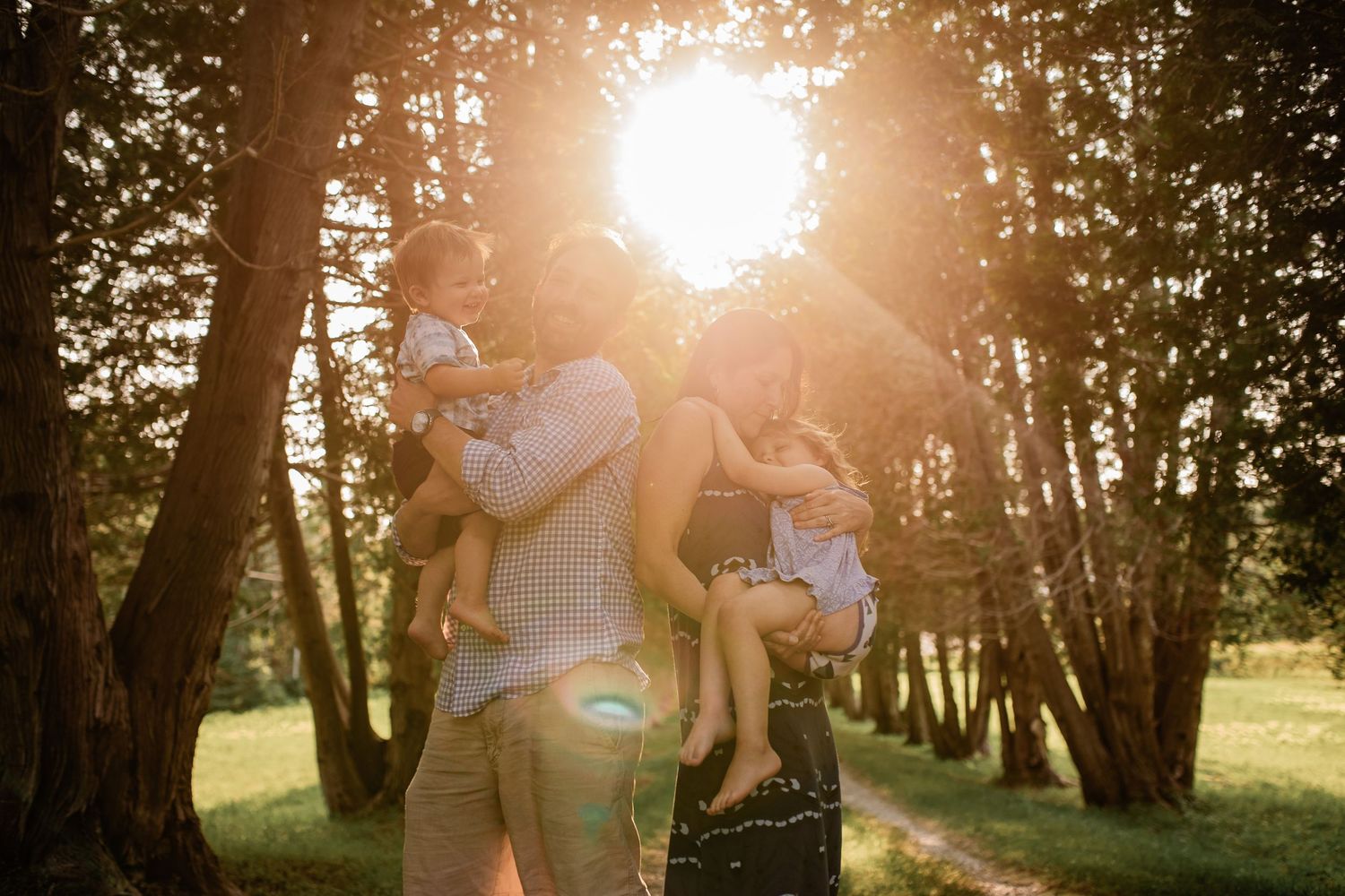 Family enjoying playful moments in a sunlit forest path during golden hour.