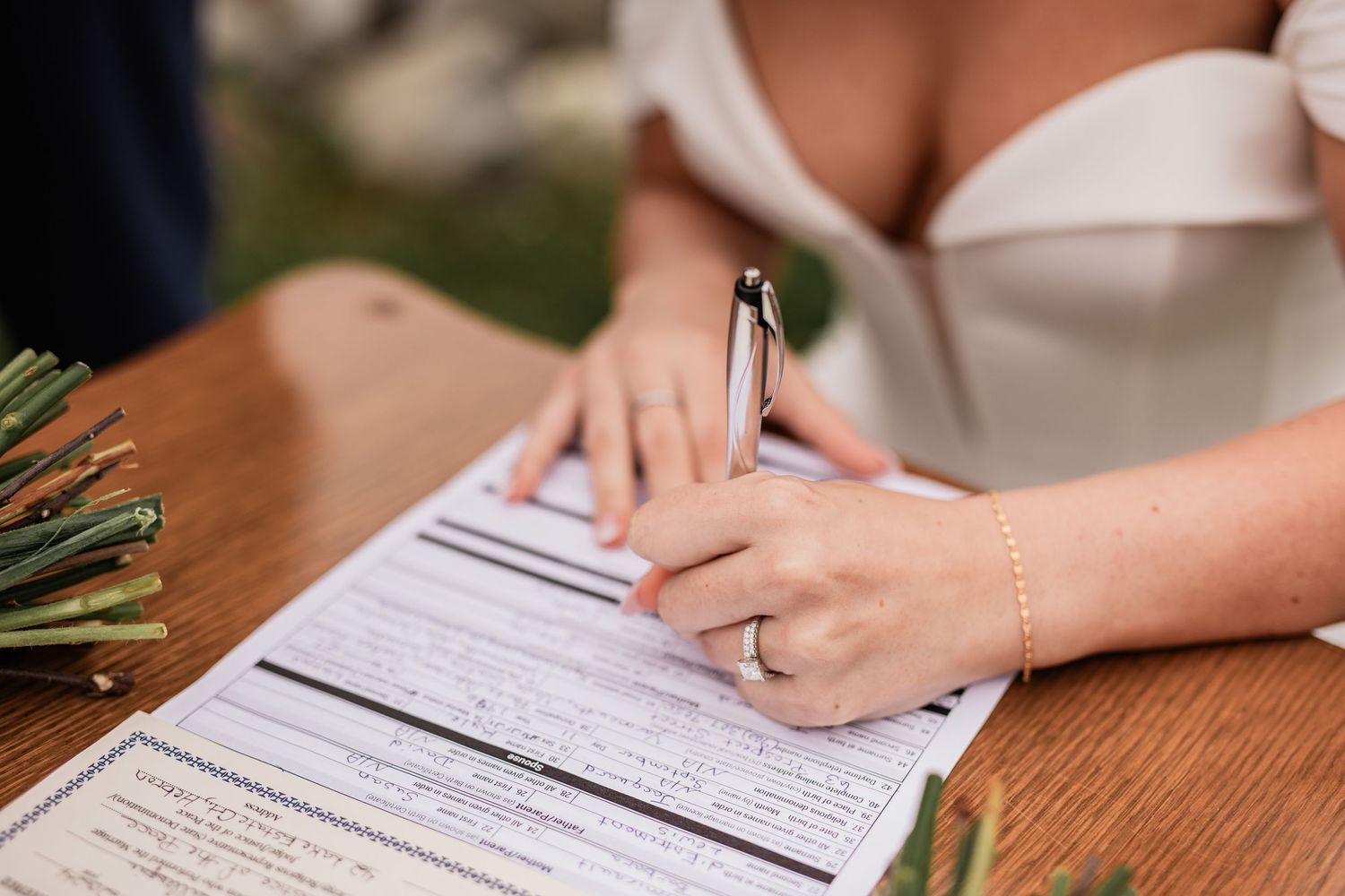 Close up of bride signing marriage license document at wooden table.