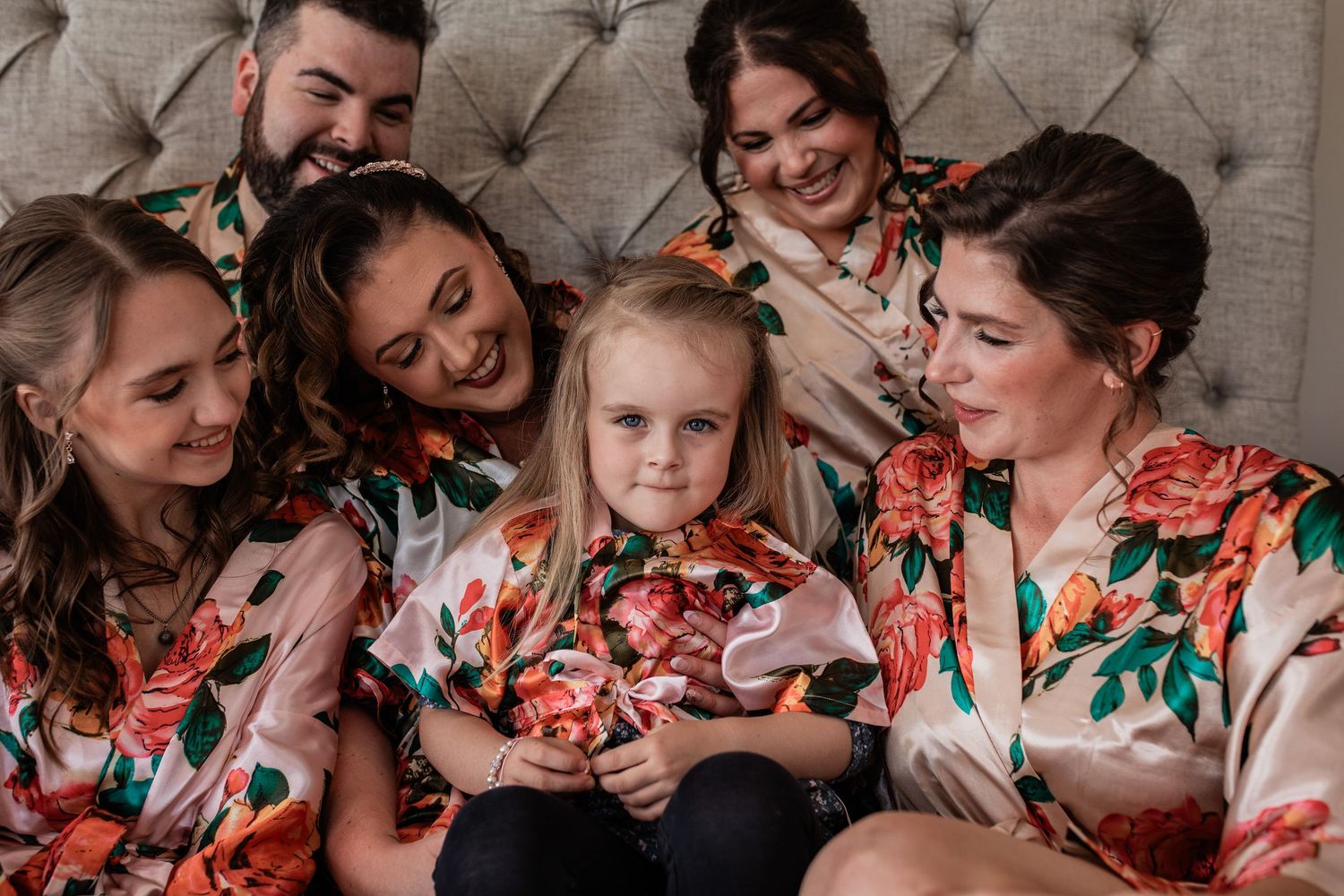 Wedding party in matching floral robes gathered on tufted headboard.