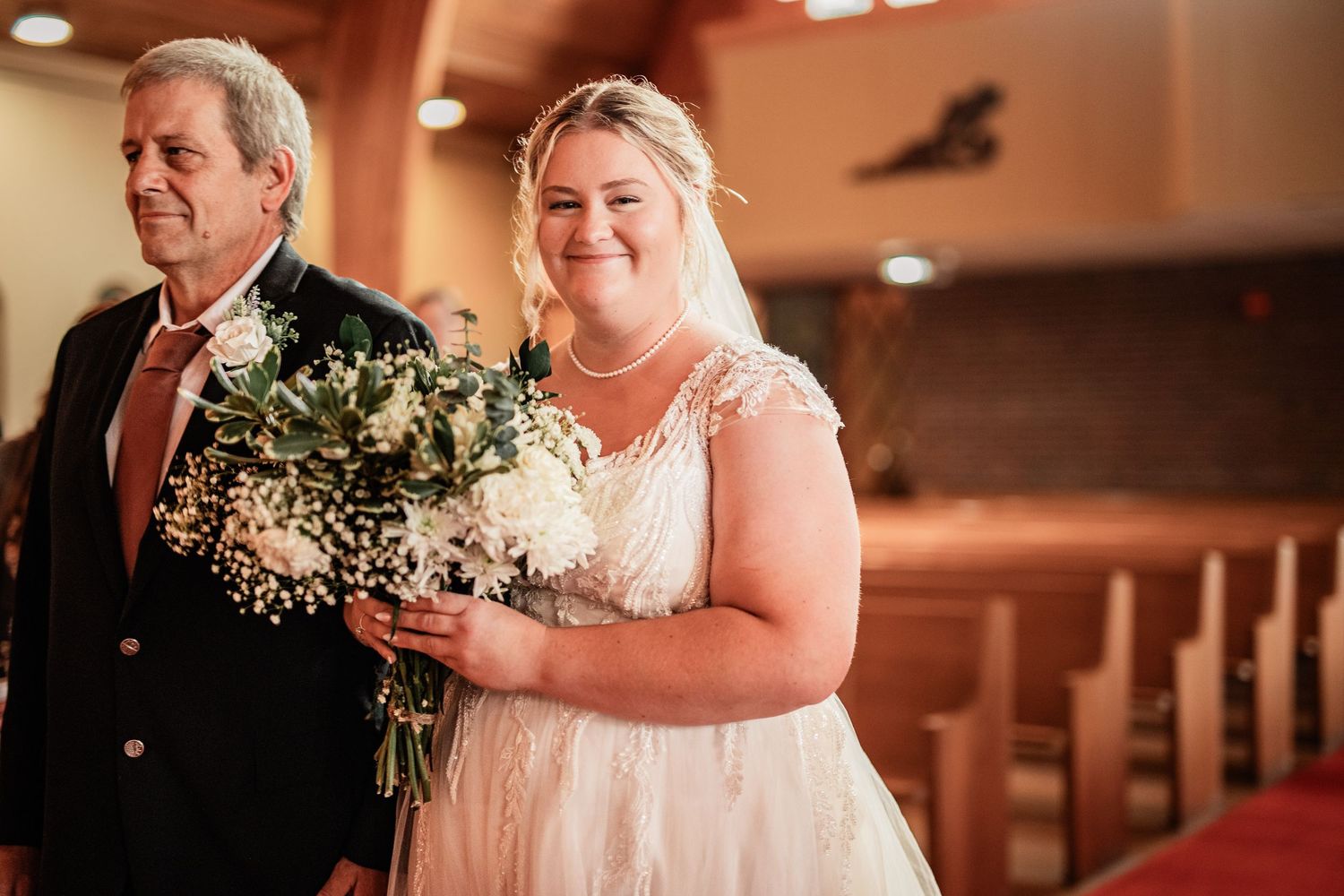 Walking down the church aisle with white floral bouquet and lace wedding dress.