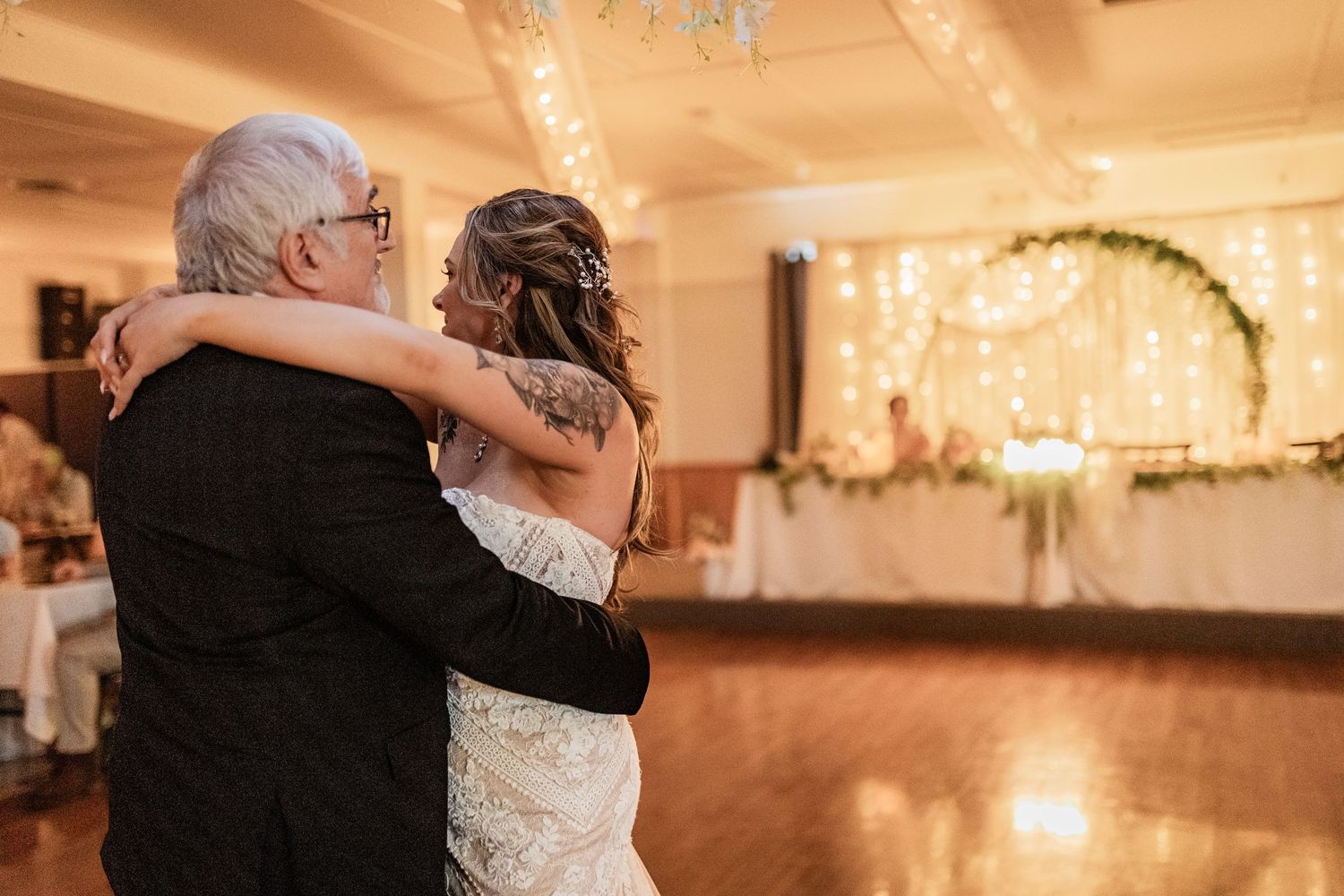 A tender dance moment in a wedding reception hall decorated with string lights and floral arches.