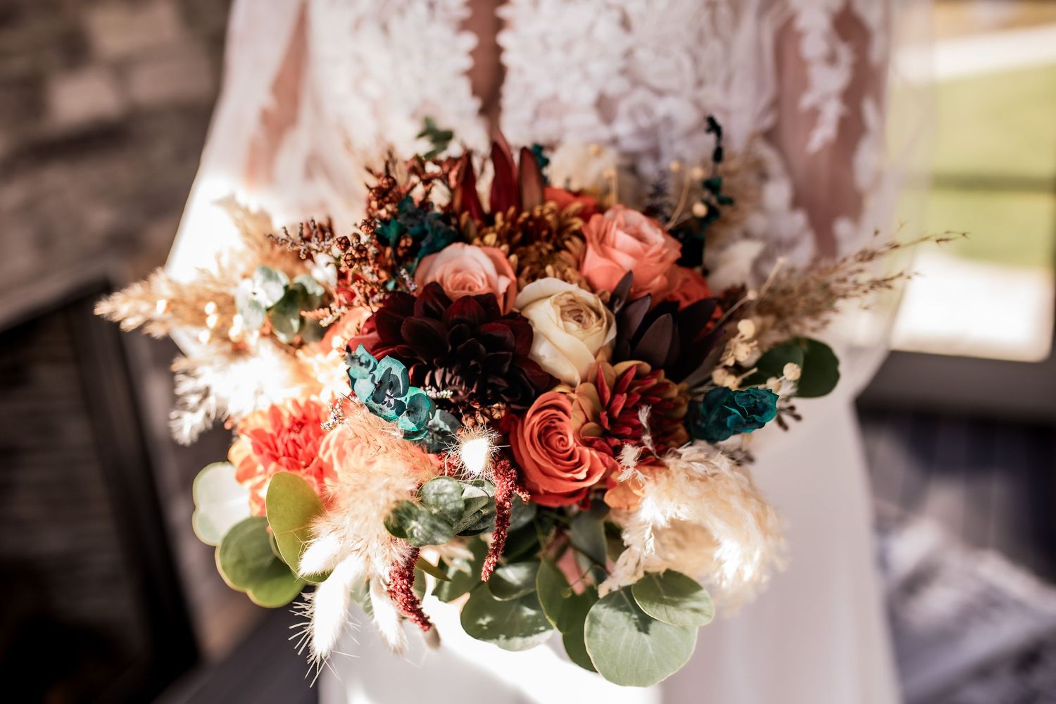 Wedding bouquet featuring coral roses, white flowers, and greenery against white dress.