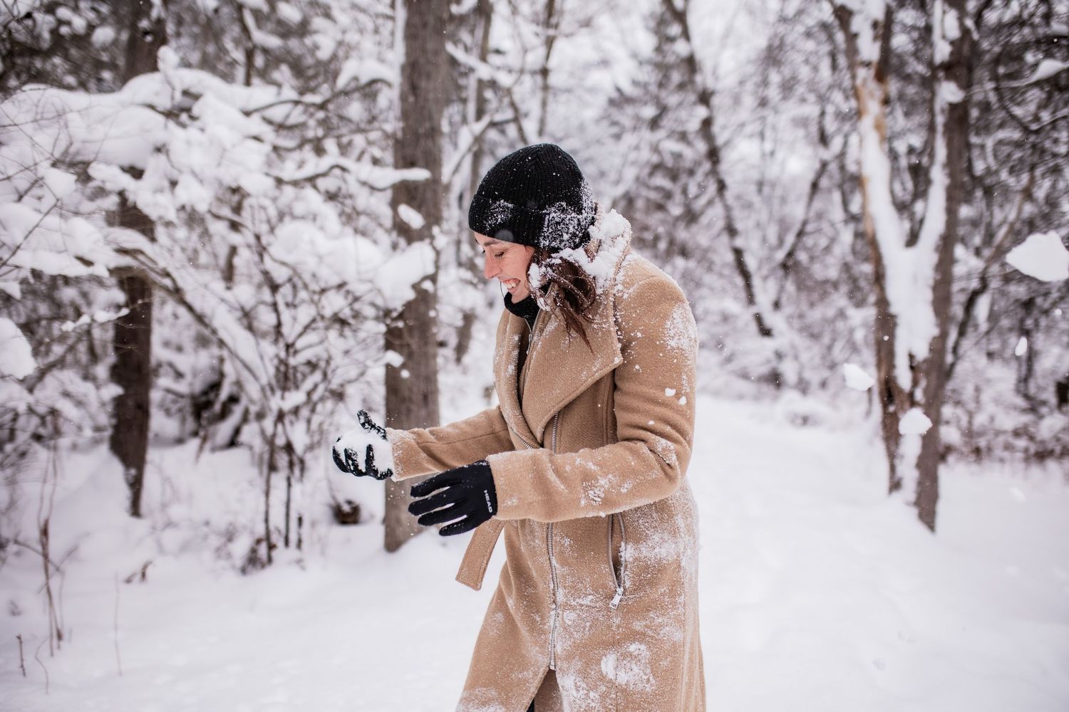 Person in a tan coat taking photos in a snowy winter forest landscape.