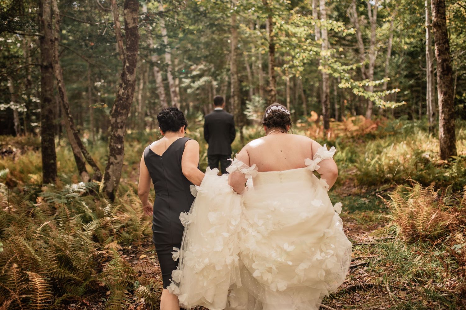 Wedding party walks through a forest path holding the bride's dress train.