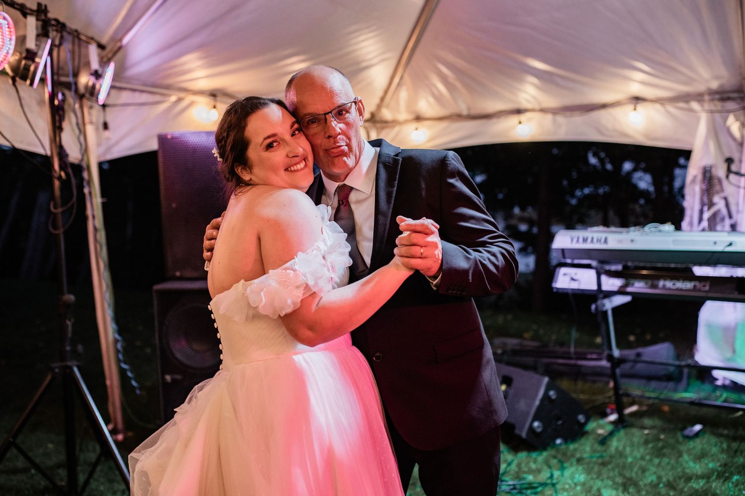 Wedding reception dance under a white tent with romantic lighting at dusk.