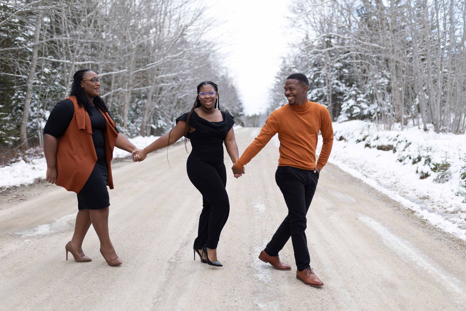 Three people holding hands while walking on a snow-covered road.