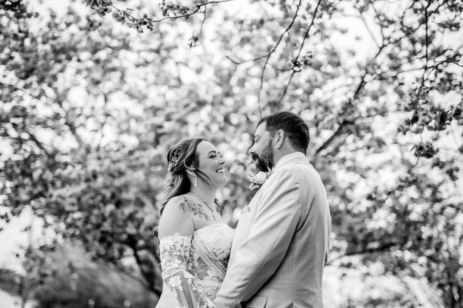 A black and white portrait of a couple sharing a tender moment under flowering trees.