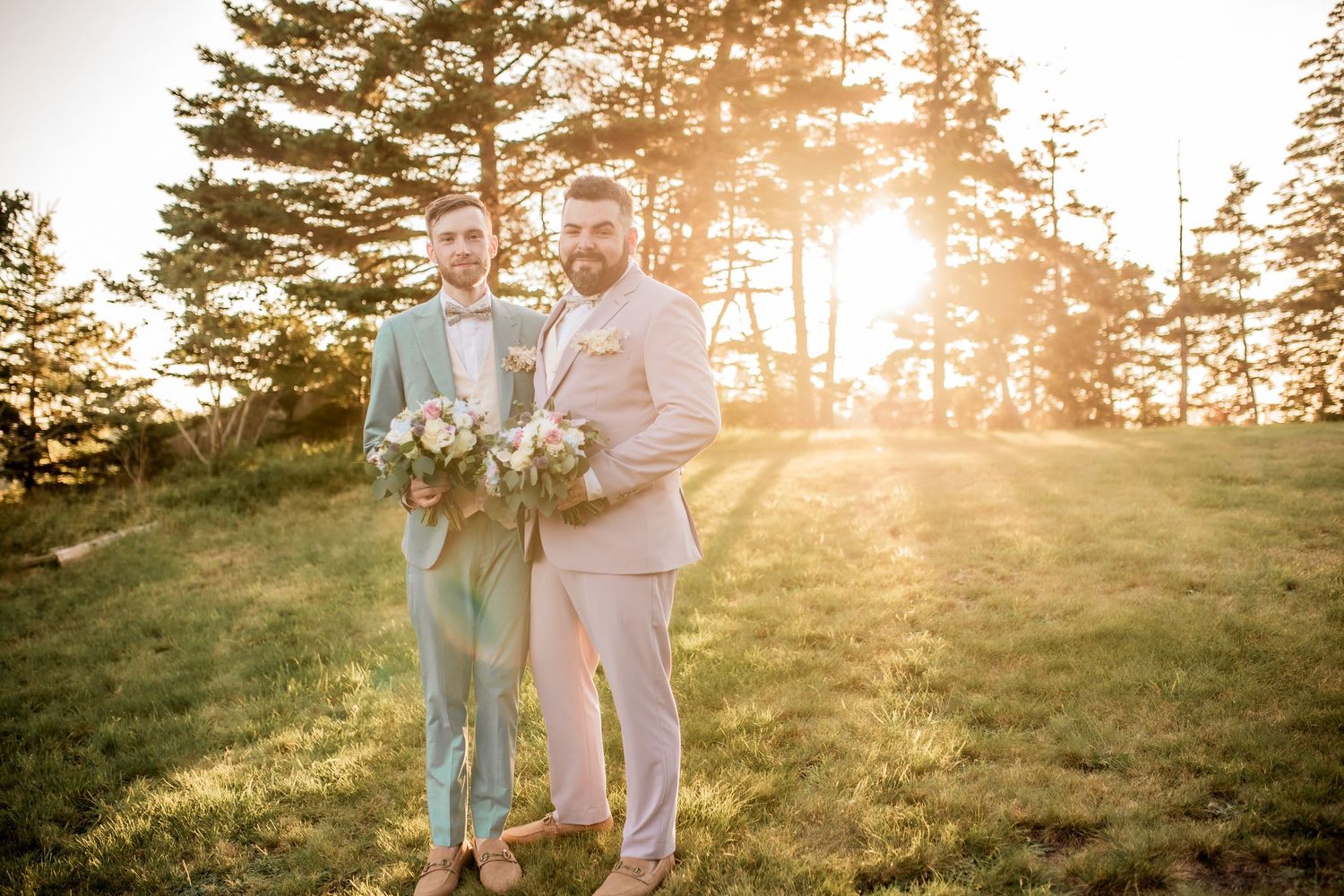 Two people posing together at sunset with pine trees and golden light in the background.