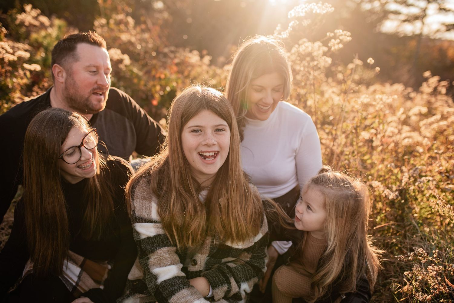 A group shares genuine laughter together during a golden hour outdoor photo session in a field of tall grass.