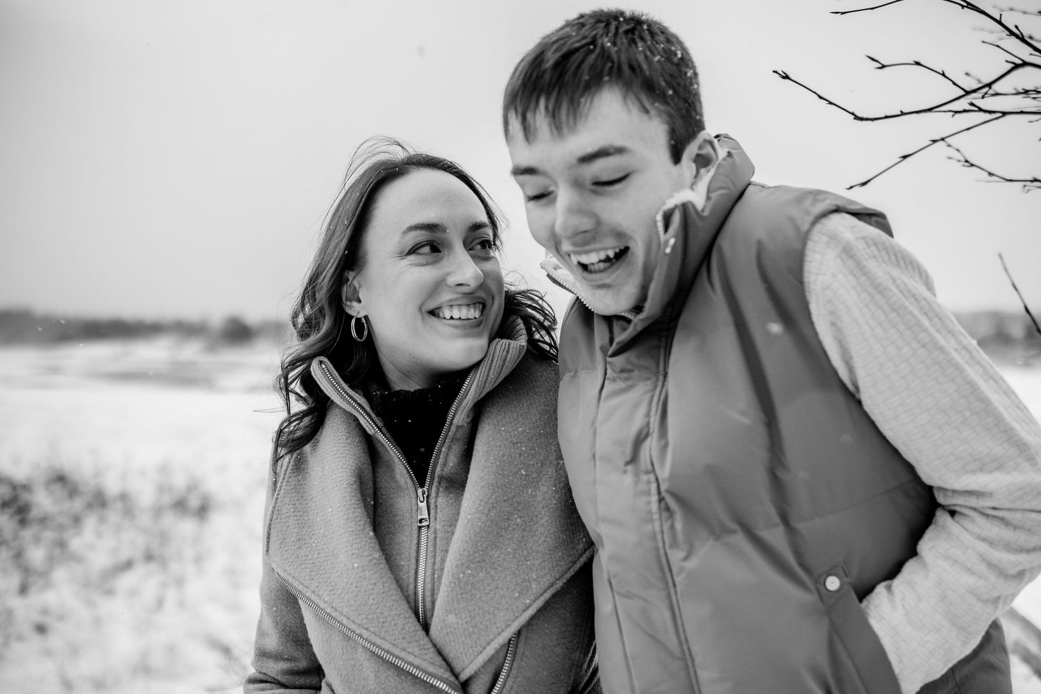 Black and white candid portrait of two people sharing a joyful moment outdoors in winter.