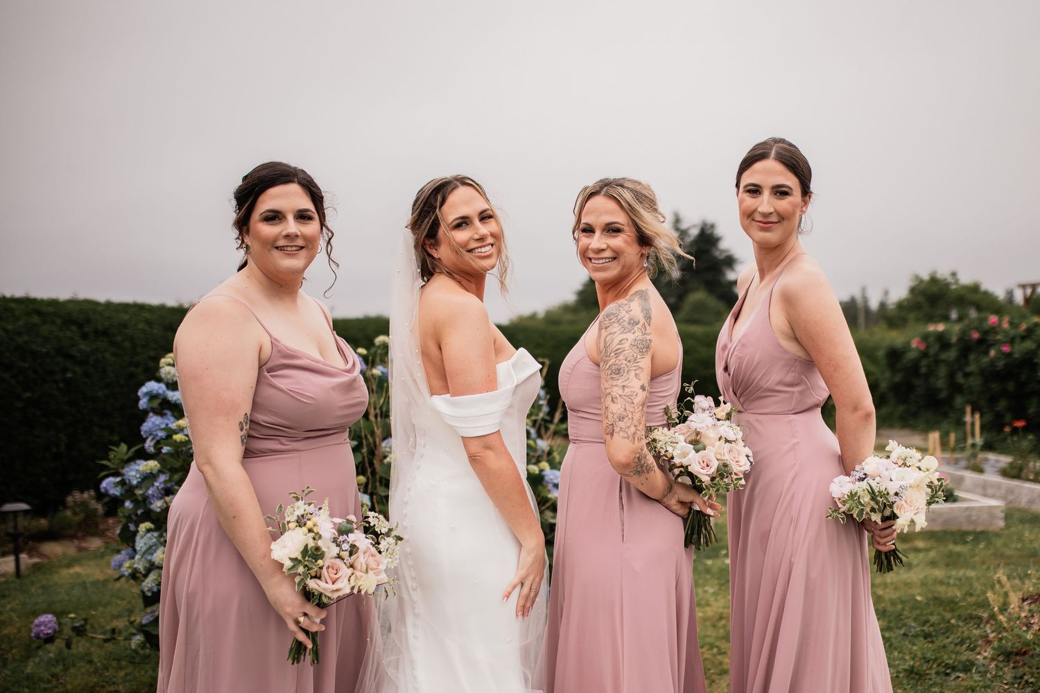 Wedding party in mauve bridesmaid dresses poses outdoors with bouquets.