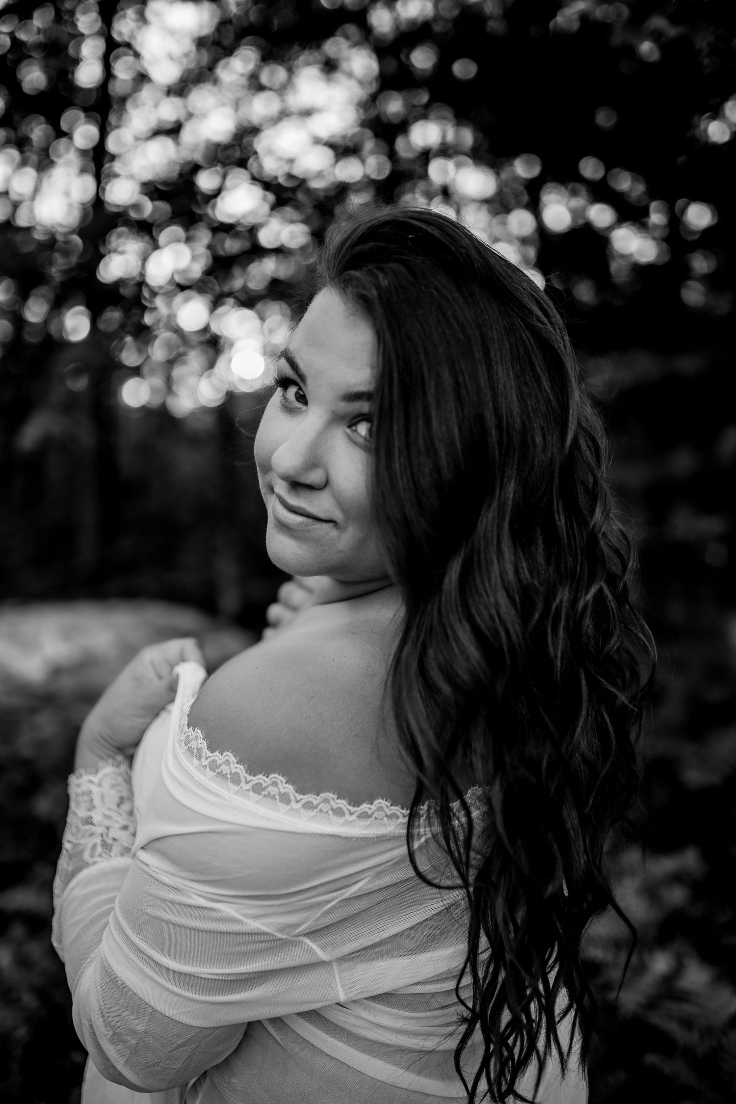 Black and white portrait shot against bokeh background showing graceful shoulder detail with delicate lace accents.