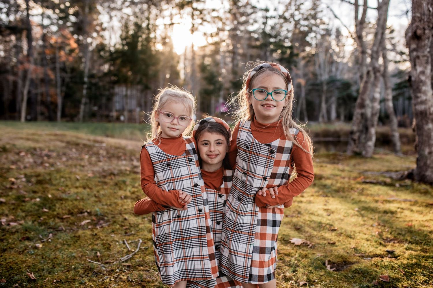 Family members in coordinated orange and plaid outfits share joyful moments in a wooded outdoor setting.
