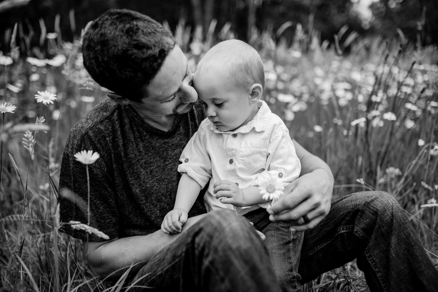 Black and white portrait of parent and child bonding in wildflower field.