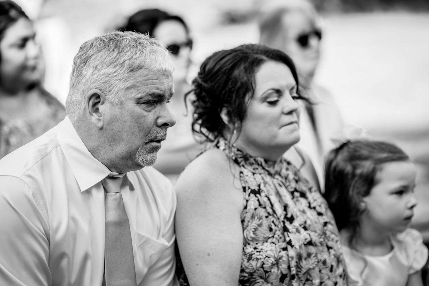Black and white candid photo of wedding guests during outdoor ceremony.