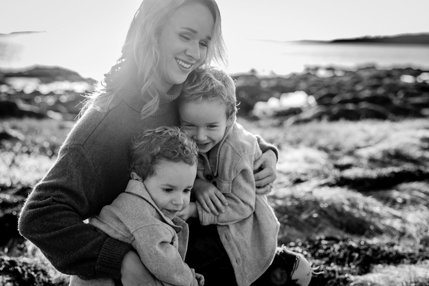 A black and white beach portrait capturing an intimate moment of embrace on rocky shores.